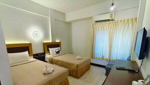 A hotel room with two beds, a desk with a TV, a phone, and a bottle of water. - Polkadot Cafe&Hotel (Phitsanulok)