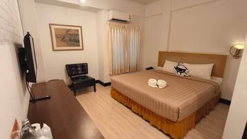 A hotel room with a bed, a desk, a chair, a television, and an air conditioning unit.