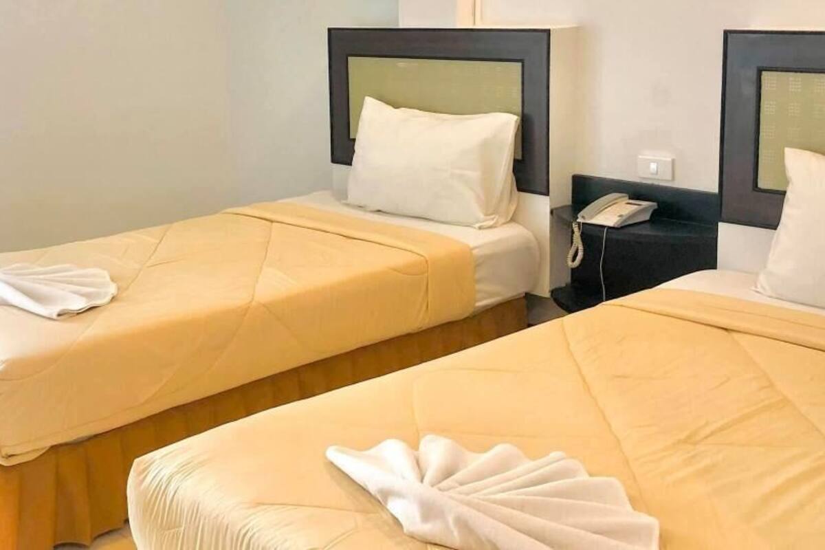Duas camas de solteiro com cabeceiras, um telefone ao lado da cama e um interruptor de luz fixado na parede.
