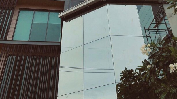 A modern building with a reflective glass facade, a corner entrance, and a visible balcony. - Polkadot Cafe&Hotel (Phitsanulok)