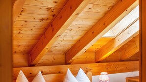 Un plafond en bois avec une lucarne, un lit avec des oreillers et une table de chevet avec une lampe.
