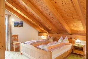 Une chambre à coucher en bois avec un plafond en pente, un lit avec une literie à rayures, une chaise, une table de chevet avec une lampe et un tableau représentant des montagnes accroché au mur.