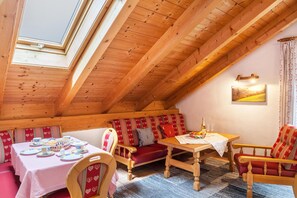 Une pièce chaleureuse avec un plafond en bois, une table à manger avec des chaises, un canapé agrémenté de coussins à motifs de cœur et un tableau accroché au mur.