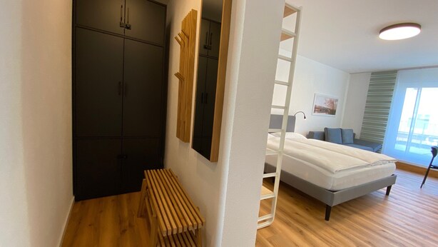 Ein Schlafzimmer mit einem Bett, einem Kleiderschrank, einer Bank, einer Leiter und einem Fenster.