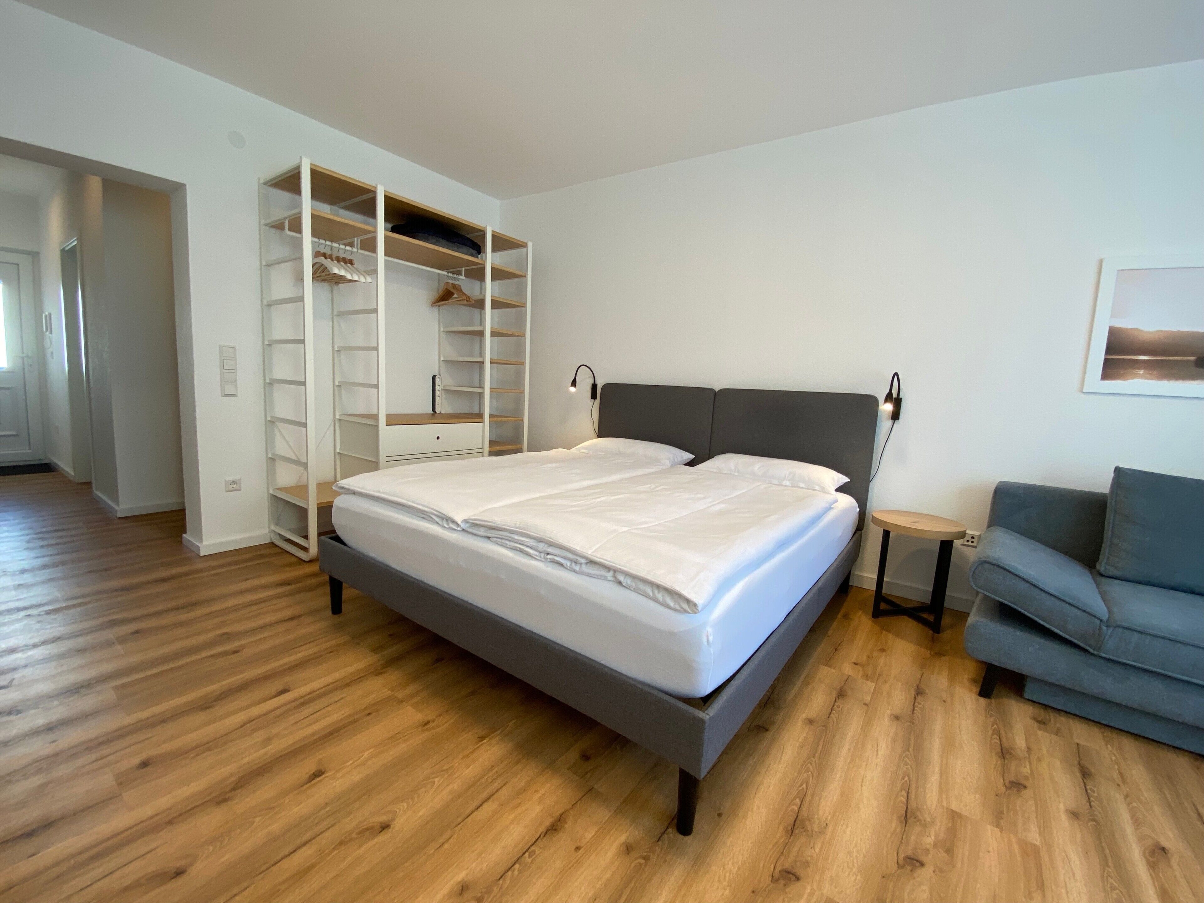 Un dormitorio con cama, un sofá gris y un vestidor con estantes.