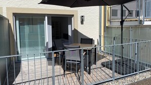 Ein Balkon mit Tisch, Stühlen und einem großen Sonnenschirm, versehen mit einem Metallgeländer.