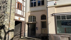 Ein Gebäude mit einer Stein-Fassade, einer Tür mit Nummernschild und einem Fenster mit Schilder.