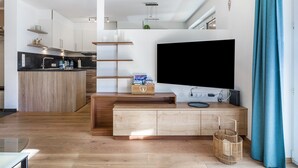 Un espace de vie moderne comprenant une cuisine, un téléviseur à écran plat et un meuble de rangement en bois pour les appareils multimédias.