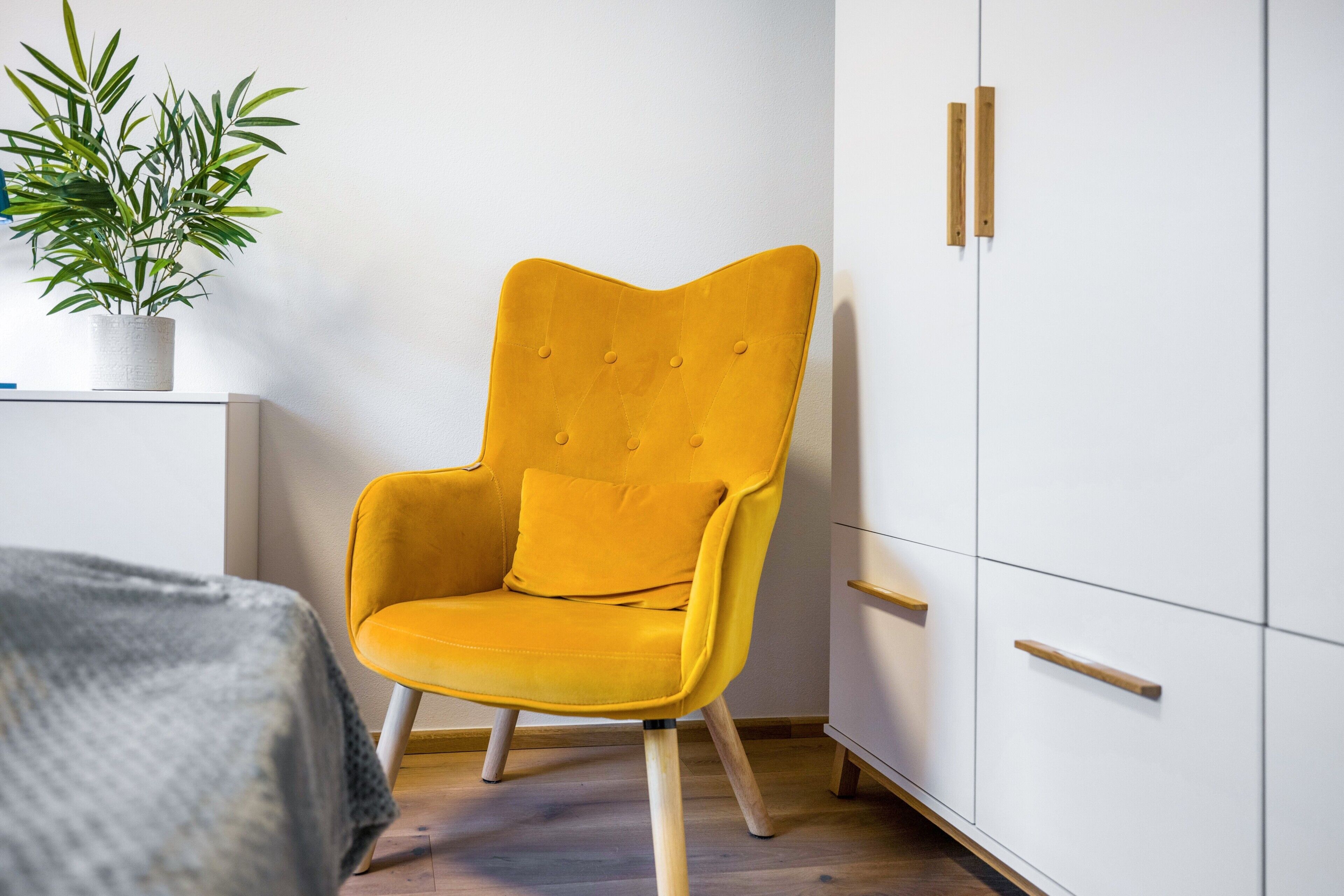 A room with a yellow armchair, a white wardrobe, and a potted plant.