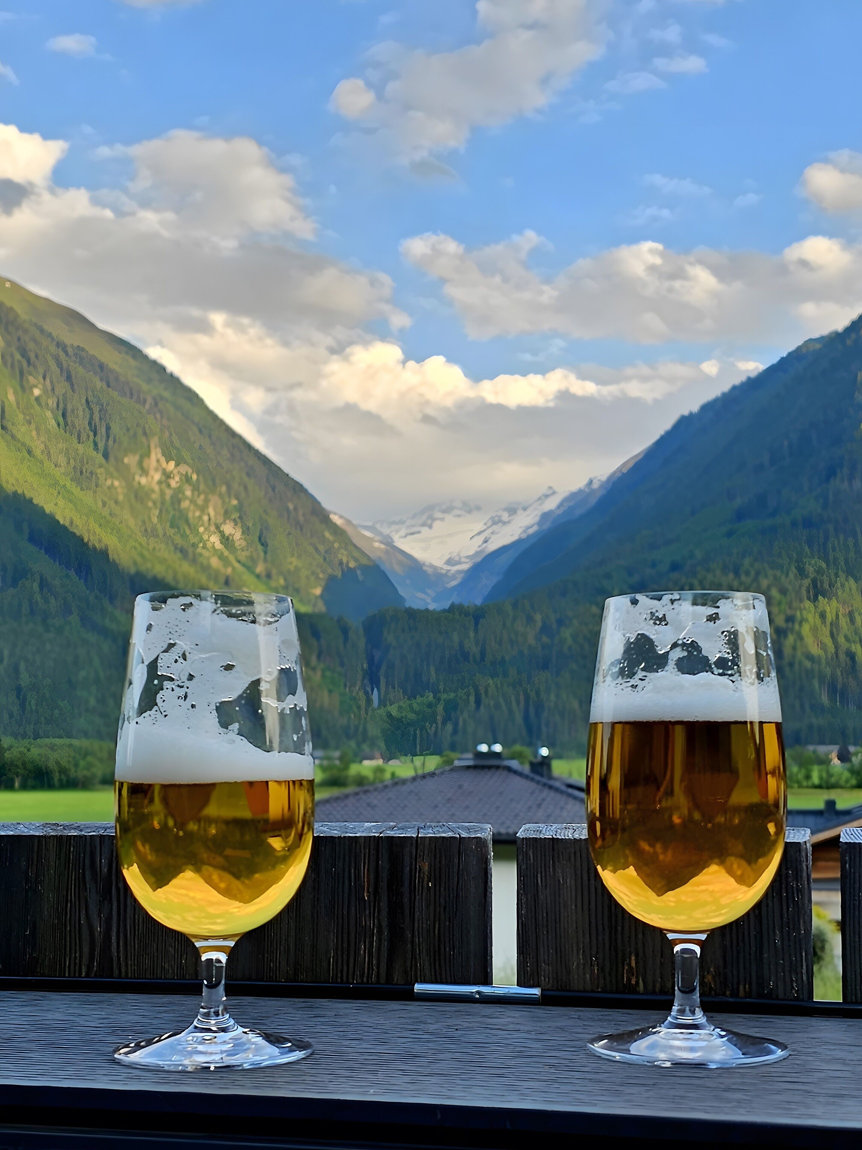 Two glasses of beer on a wooden surface with a mountain view in the background.