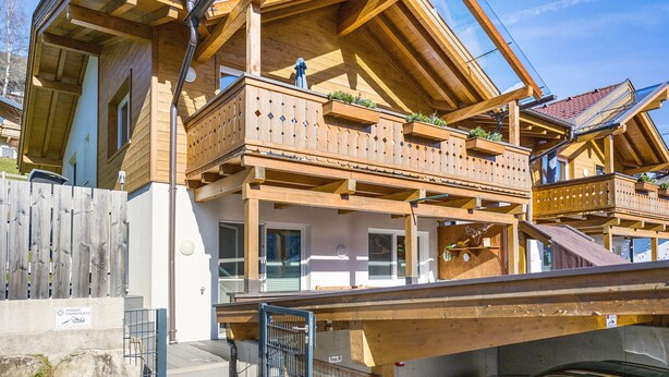 Un chalet en bois doté d’un balcon, d’une terrasse en bois et d’une voiture garée devant.