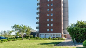 Un edificio de varios pisos de ladrillo con techo plano, una entrada central y un estacionamiento con aparcamiento techado.