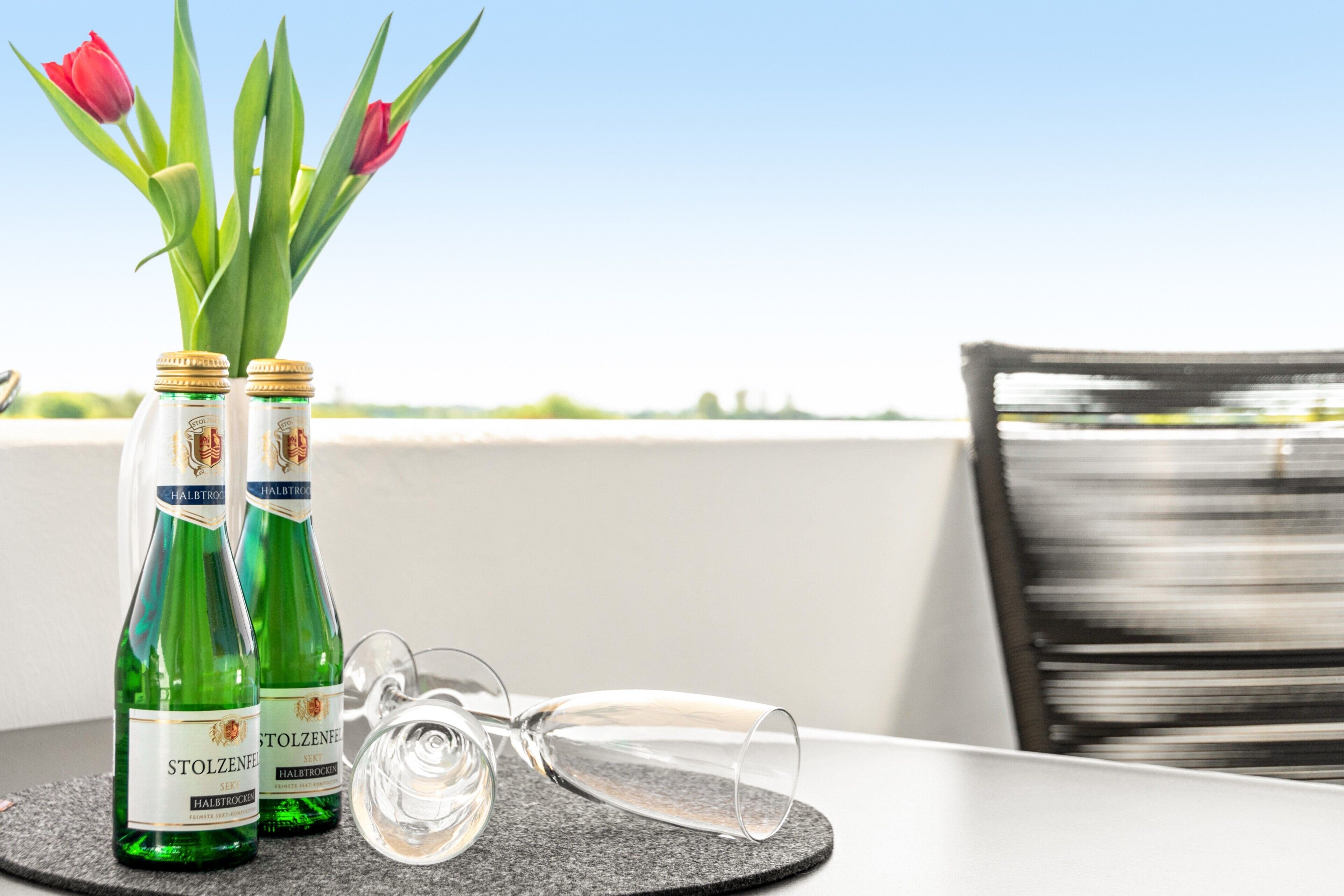 Zwei Flaschen Stolzenfelfl Wein, ein Glas und eine Vase mit Tulpen auf einem Tisch.