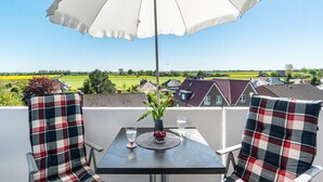 Un balcón con una mesa, dos sillas, un parasol blanco y vistas a un paisaje rural.