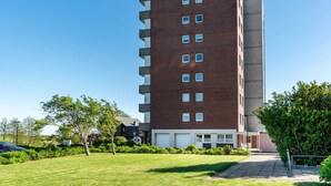 Un edificio de varios pisos de ladrillo con techo plano, una zona de estacionamiento y un césped bien cuidado.