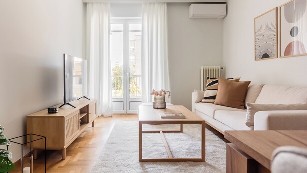 A modern living room with a wooden TV stand, a white sofa, a coffee table, and a large window with curtains. - Graceful 2BR Apartment in Paleo Faliro (Paleo Faliro)