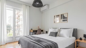 A modern bedroom with a large bed, a desk, and a view of the outside balcony. - Graceful 2BR Apartment in Paleo Faliro (Paleo Faliro)