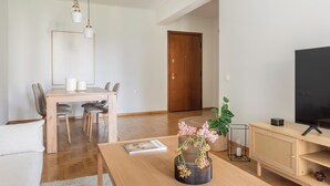 A modern living room with a wooden dining table, chairs, a sofa, a TV, and decorative items. - Graceful 2BR Apartment in Paleo Faliro (Paleo Faliro)