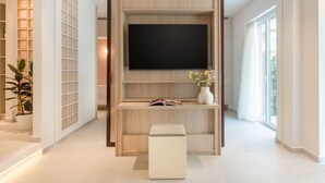 A modern living room with a large flat-screen TV mounted on a wooden wall, a small white ottoman, a potted plant, and a vase with flowers. - Culture Retreat 1 near Archaeological Museum (Athina)