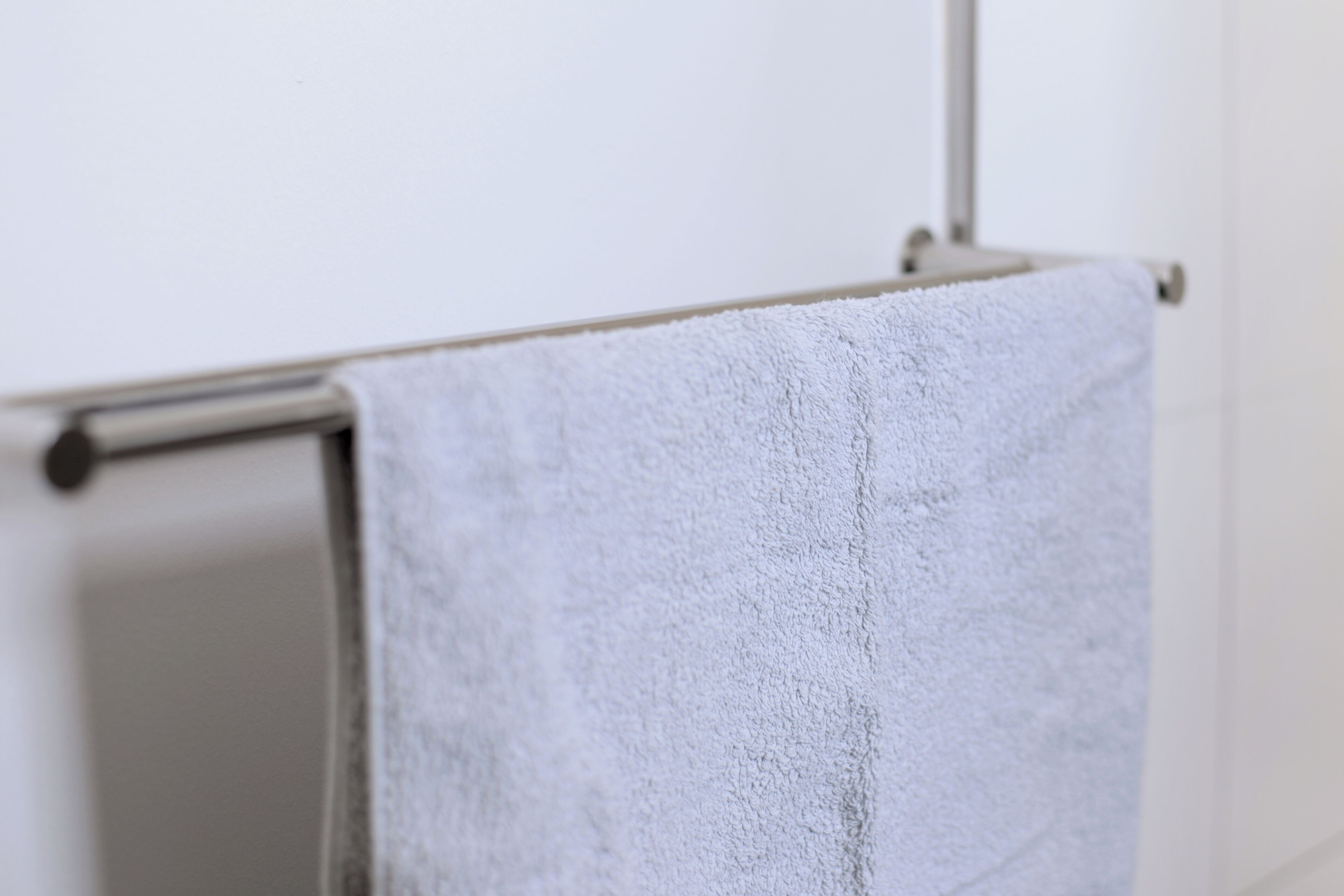 A white towel hanging on a metal towel rack in a bathroom.