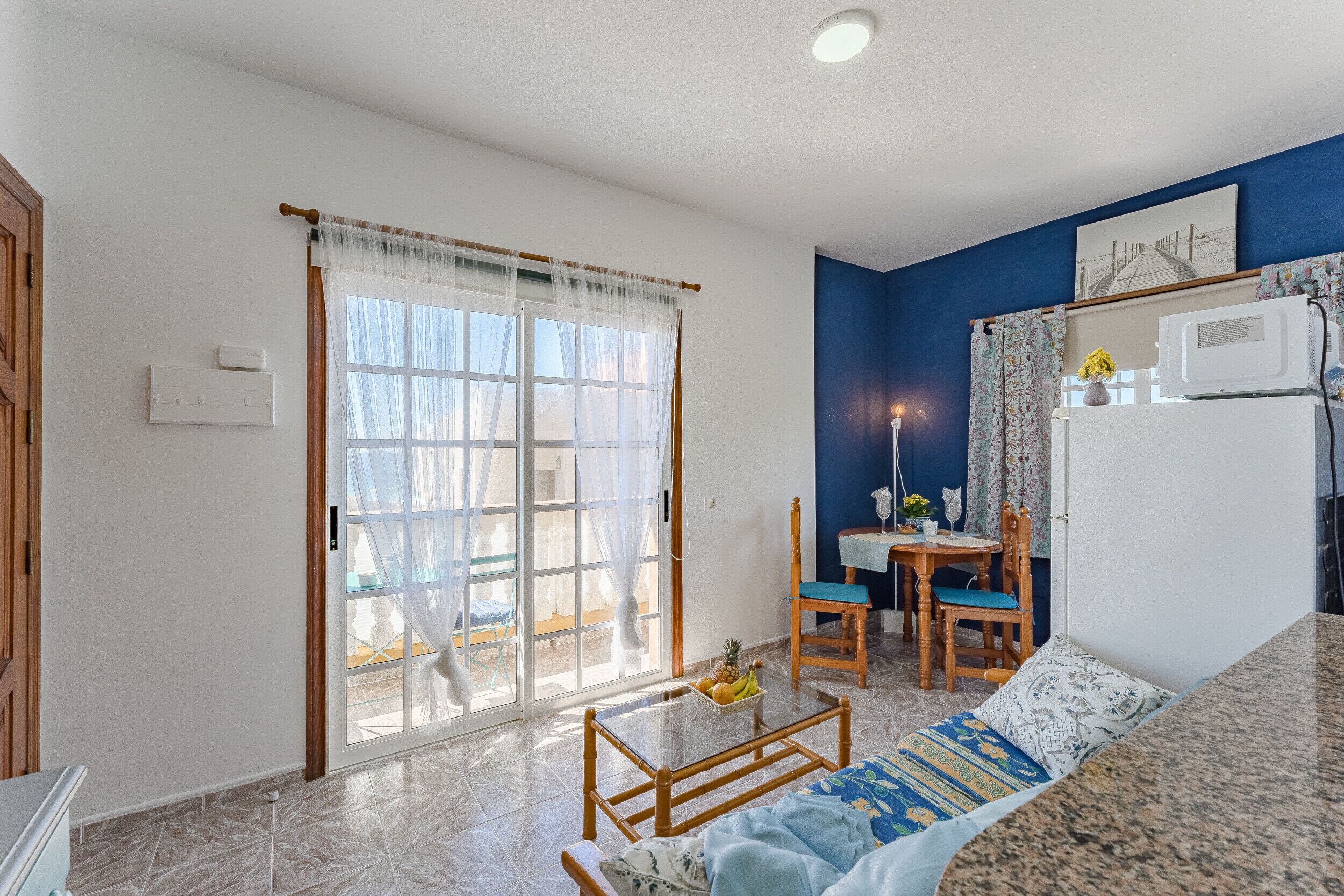 A compact living space with a sofa, a dining table with chairs, a kitchen area with a microwave, and a sliding glass door leading to an outdoor area.