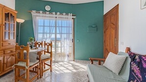 A room with a dining table, chairs, a sofa, a wooden cabinet, and a large window with curtains.