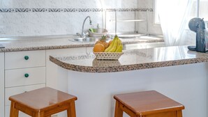 A kitchen with a granite countertop, a fruit basket, and two wooden stools.