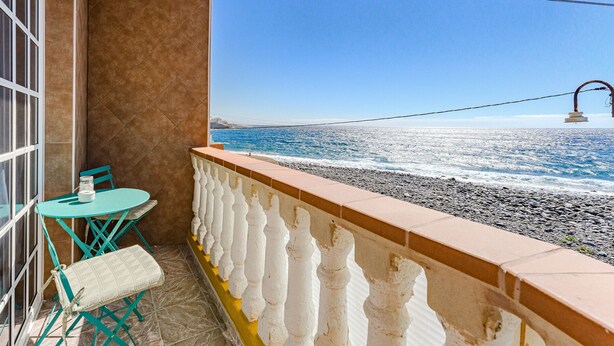 A balcony with a view of the sea, a table with chairs, and a bench.