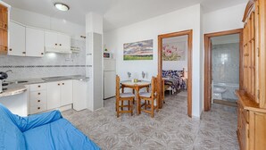 Eine kompakte Küche mit weißen Schränken, einem Esstisch mit Stühlen und einem durchgehenden Türbogen einsehbarer Badezimmer.