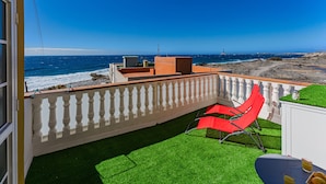 Ein Balkon mit Meerblick, ein roter Stuhl und Kunstrasen.