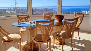 Ein Essbereich mit Tisch und Stühlen, große Fenster mit Blick auf Stadt und Meer, und Pendelleuchten.