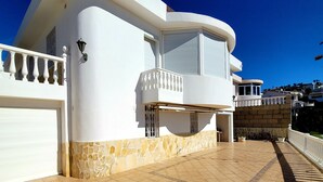 Ein modernes, zweistöckiges Haus mit einer geschwungenen Fassade, einem Steinfundament und einem Balkon mit weißer Brüstung.
