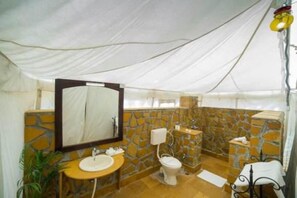 A bathroom with a stone wall, a sink, a toilet, and a mirror. - Golden Rose Heritage Desert Safari Camp  (Jaisalmer)