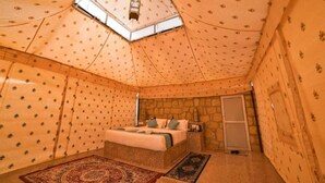 A cozy, tent-like room with a bed, a stone wall, and a skylight. - Golden Rose Heritage Desert Safari Camp  (Jaisalmer)