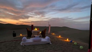 A desert setting with a table set for two, surrounded by sand dunes, under a twilight sky. - Golden Rose Heritage Desert Safari Camp  (Jaisalmer)