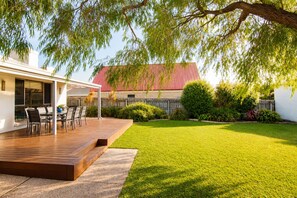 A patio with outdoor furniture, a lawn, and a building with a red roof. - Gifford Getaway (Dunsborough)