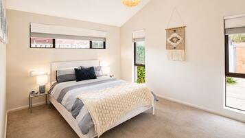 Quarto com cama, mesas de cabeceira, luminária pendente, janela e um painel de macramé na parede.