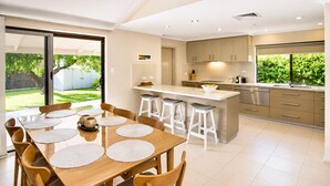 A modern kitchen with a dining area, large windows, and a view of greenery. - Gifford Getaway (Dunsborough)