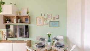 A dining area with a glass table, white chairs, and a TV mounted on the wall.