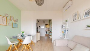 A modern living room with a sofa, dining table, chairs, and a kitchen in the background.