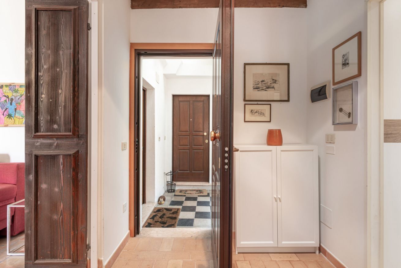 A hallway with a wooden door, a white cabinet, and a checkered mat leading to a room.