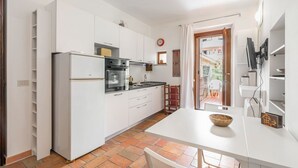 A compact kitchen with white cabinets, a refrigerator, a stove, and a dining area with a table and chairs.
