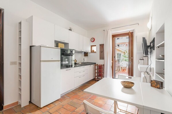 A compact kitchen with white cabinets, a refrigerator, a stove, and a dining area with a table and chairs.