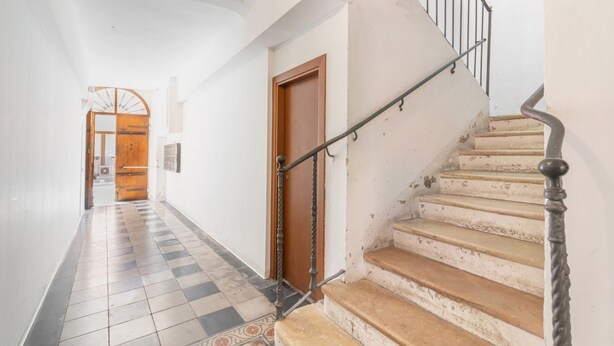A staircase with a metal handrail leading to a wooden door, a tiled floor with a geometric pattern, and a white wall.