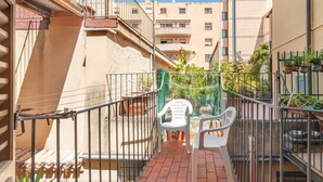 A balcony with a metal railing, a white plastic chair, and potted plants.