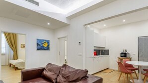 A modern living room with a brown leather sofa, a dining area with a white table and red chairs, a kitchen with white cabinets, and a painting on the wall. - GuestHost - Modern 80 sqm apartment, able to comfortably accommodate up to 6 people, located on the basement floor. The property is located in the Statuto area, just outside the centre, a 5-minute walk from the Fortezza Garden and 10 minutes from the For (Firenze)