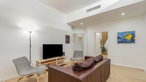 A modern living room with a flat-screen TV, a sofa, a chair, and artwork on the wall. - GuestHost - Modern 80 sqm apartment, able to comfortably accommodate up to 6 people, located on the basement floor. The property is located in the Statuto area, just outside the centre, a 5-minute walk from the Fortezza Garden and 10 minutes from the For (Firenze)