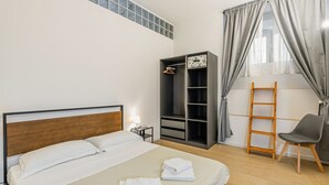 A hotel room with a bed, wardrobe, chair, and a ladder. - GuestHost - Modern 80 sqm apartment, able to comfortably accommodate up to 6 people, located on the basement floor. The property is located in the Statuto area, just outside the centre, a 5-minute walk from the Fortezza Garden and 10 minutes from the For (Firenze)