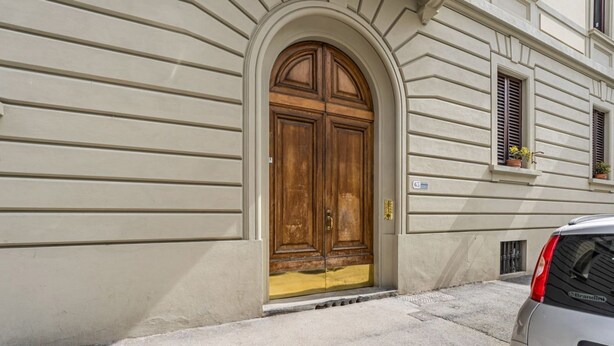 A building with a large wooden double door, a small window with shutters, and a car parked in front. - GuestHost - Modern 80 sqm apartment, able to comfortably accommodate up to 6 people, located on the basement floor. The property is located in the Statuto area, just outside the centre, a 5-minute walk from the Fortezza Garden and 10 minutes from the For (Firenze)