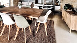 A spacious dining area with a wooden table and chairs, a kitchen in the background, and a stone wall. - La Grange aux Souvenirs - Perigord Noir (Les Coteaux Périgourdins)